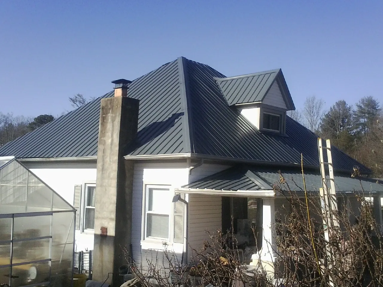 Dark blue standing seam metal roof on a white farmhouse with dormer — Slate & Tile Roof Repair by Roofing Brothers in West Warren