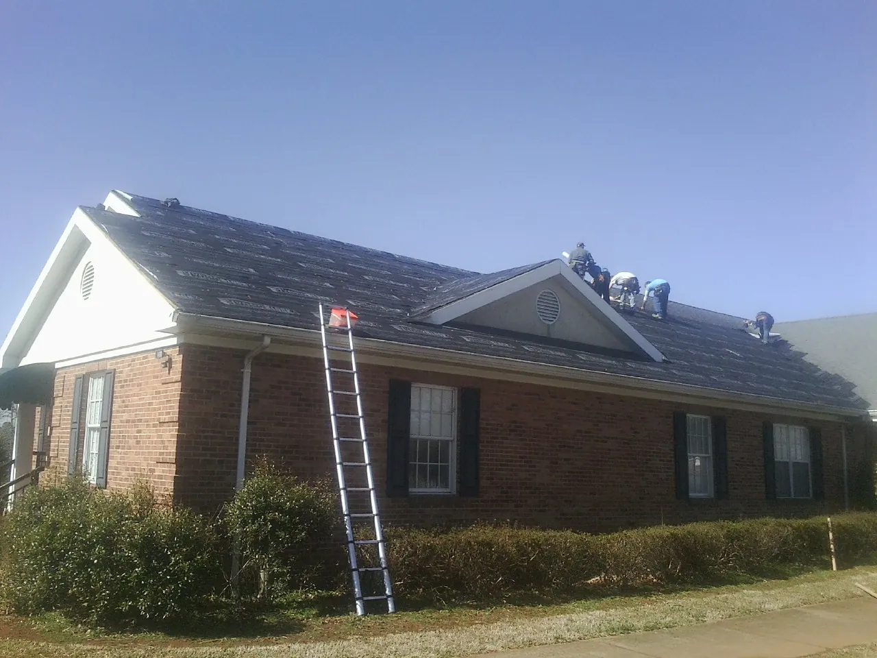 Crew tearing shingles off a brick ranch roof with a ladder set — Metal Roof Repair work by our crew in West Warren