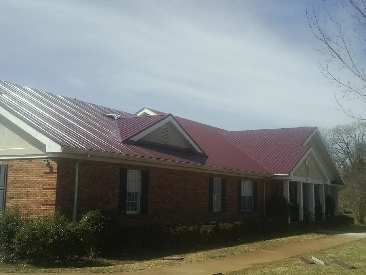 Red metal roof with gabled entries on a long brick building, from a Hail Damage Roof Repair job in West Warren