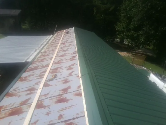 Old rusted panels beside newly installed green metal roofing — Wind Damage Roof Repair by Roofing Brothers in West Warren