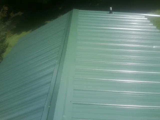 New green metal panels meeting at the ridge of a roof — Flat Roof Repair work by our crew in West Warren