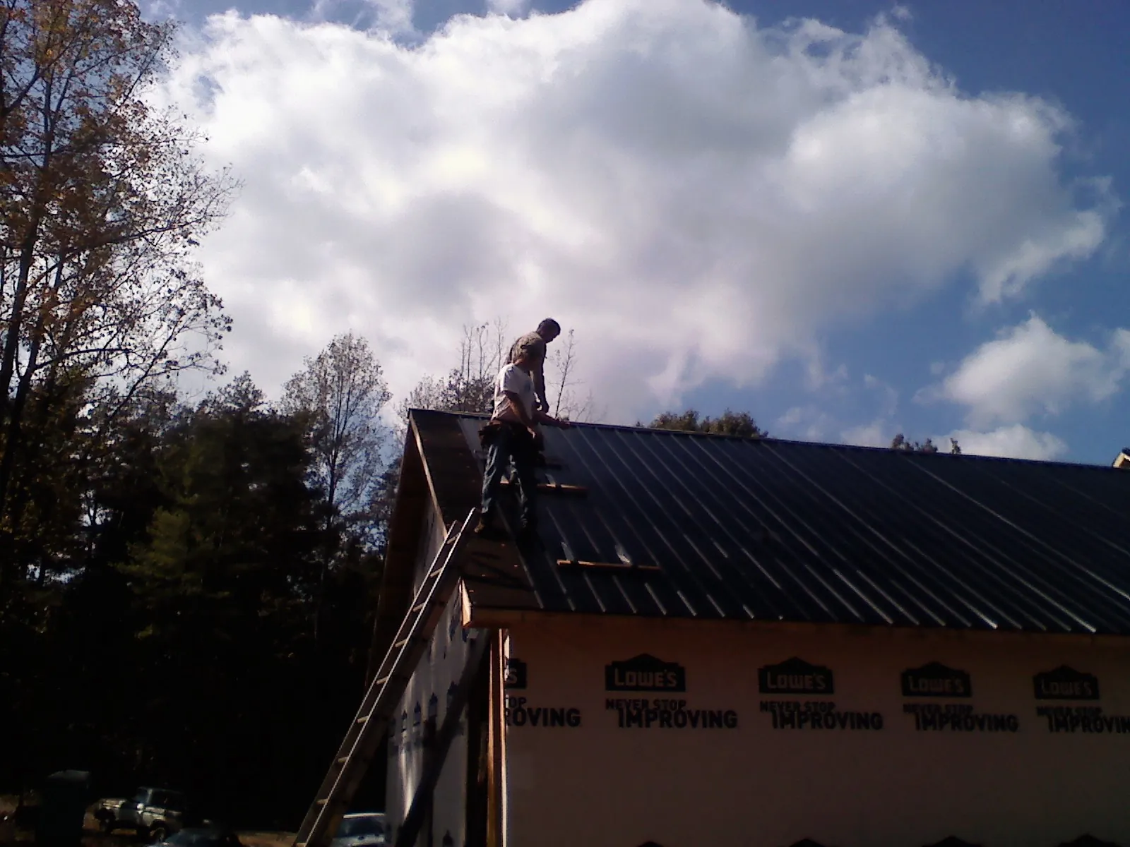 Roofer fastening dark metal panels high against a cloudy sky, from a Roof Inspection job in West Warren