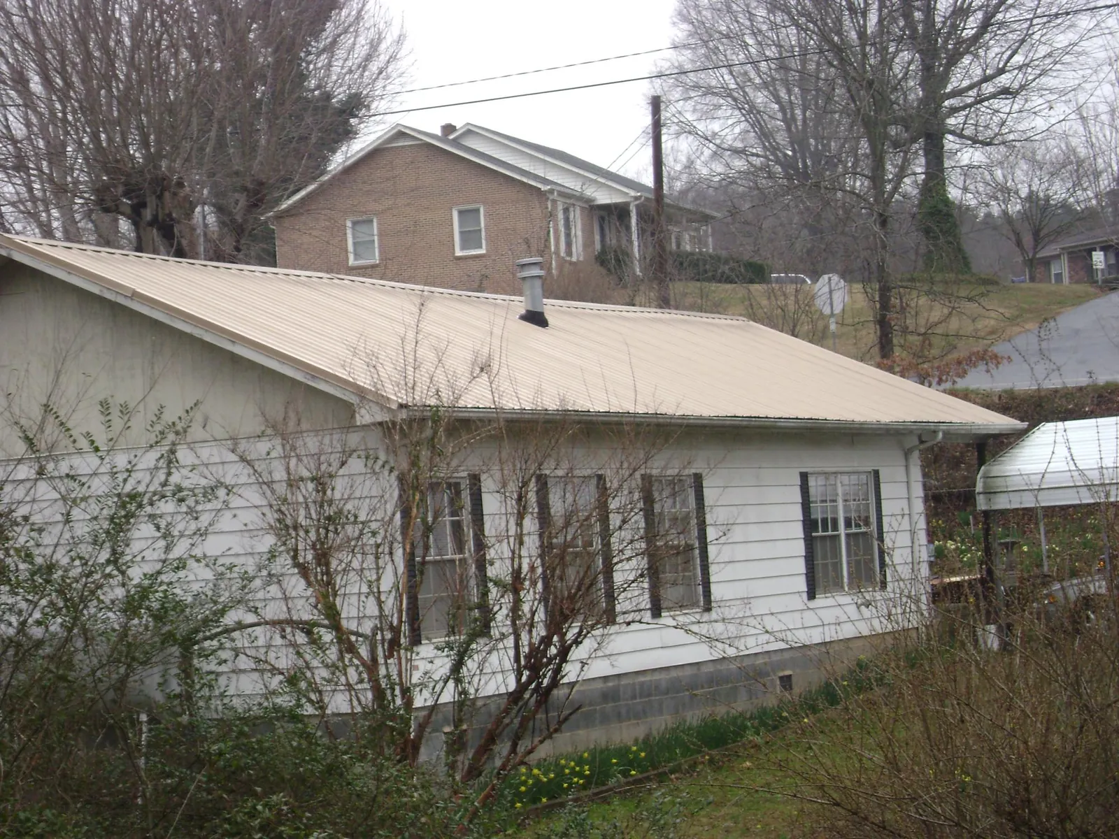 Tan metal roof on a white sided house set into a hillside — Commercial Roofing by Roofing Brothers in West Warren