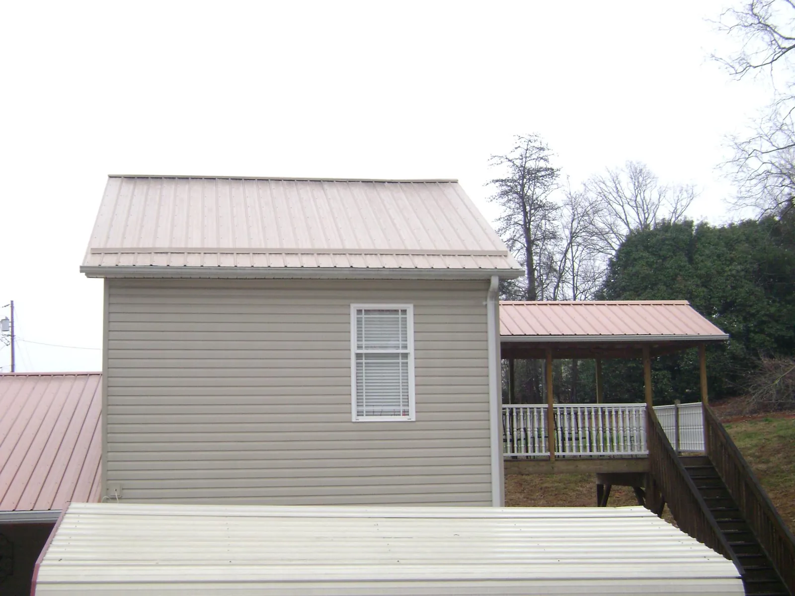Tan metal roofs on a two story addition and attached porch, from a Roof Replacement job in West Warren